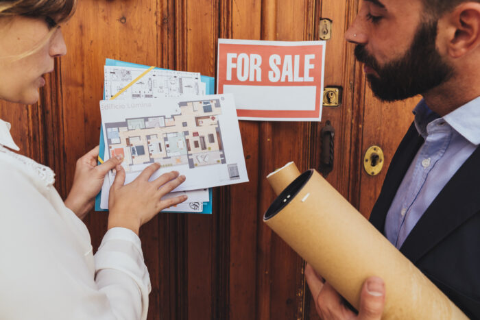 Surveyors reviewing building plans in front of a property for sale.